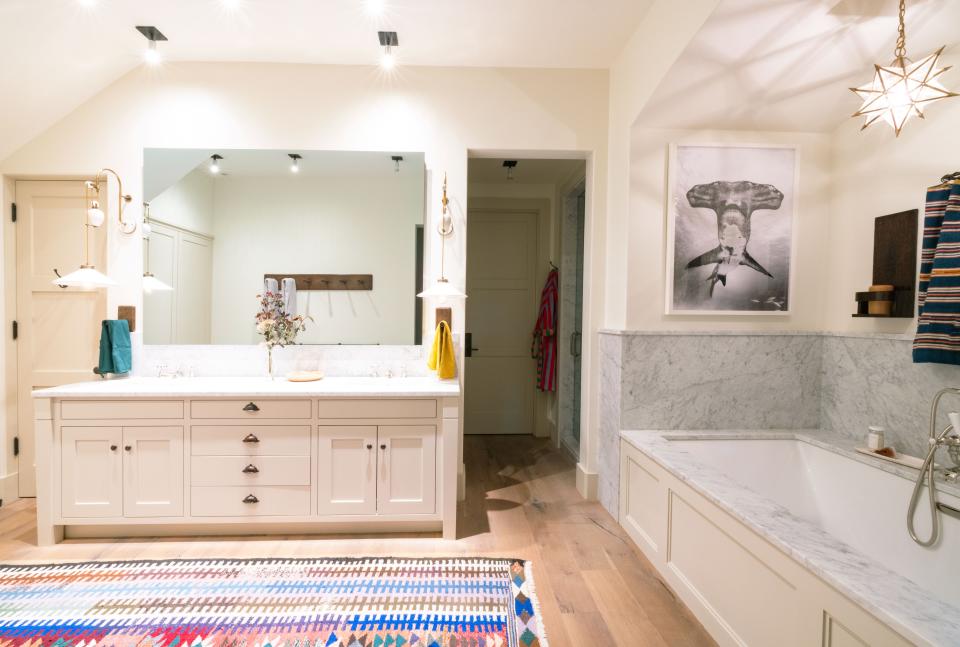 More custom woodwork is found in the primary bathroom, this time in the form of towel hooks and wall shelves. There are also Dusen Dusen towels from Coming Soon NY, a star-shaped light fixture from Vaughan, and another Carol Piper rug.