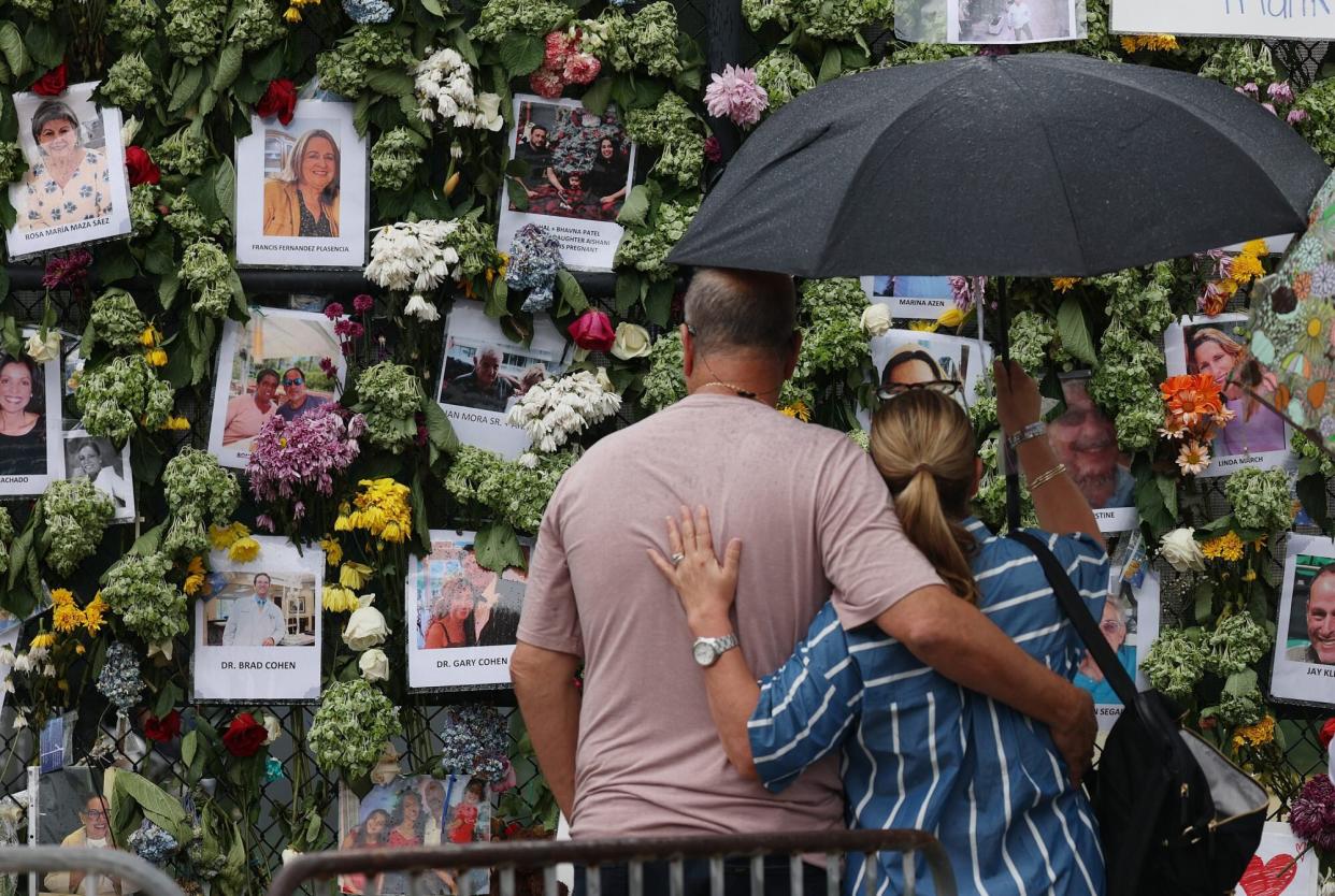 SURFSIDE, FLORIDA - JUNE 30: People look at a memorial that has pictures of some of the missing from the partially collapsed 12-story Champlain Towers South condo building on June 30, 2021 in Surfside, Florida. The pictures were placed on the fence as loved ones try to find them. Over one hundred people are being reported missing as the search-and-rescue effort continues. (Photo by Joe Raedle/Getty Images)