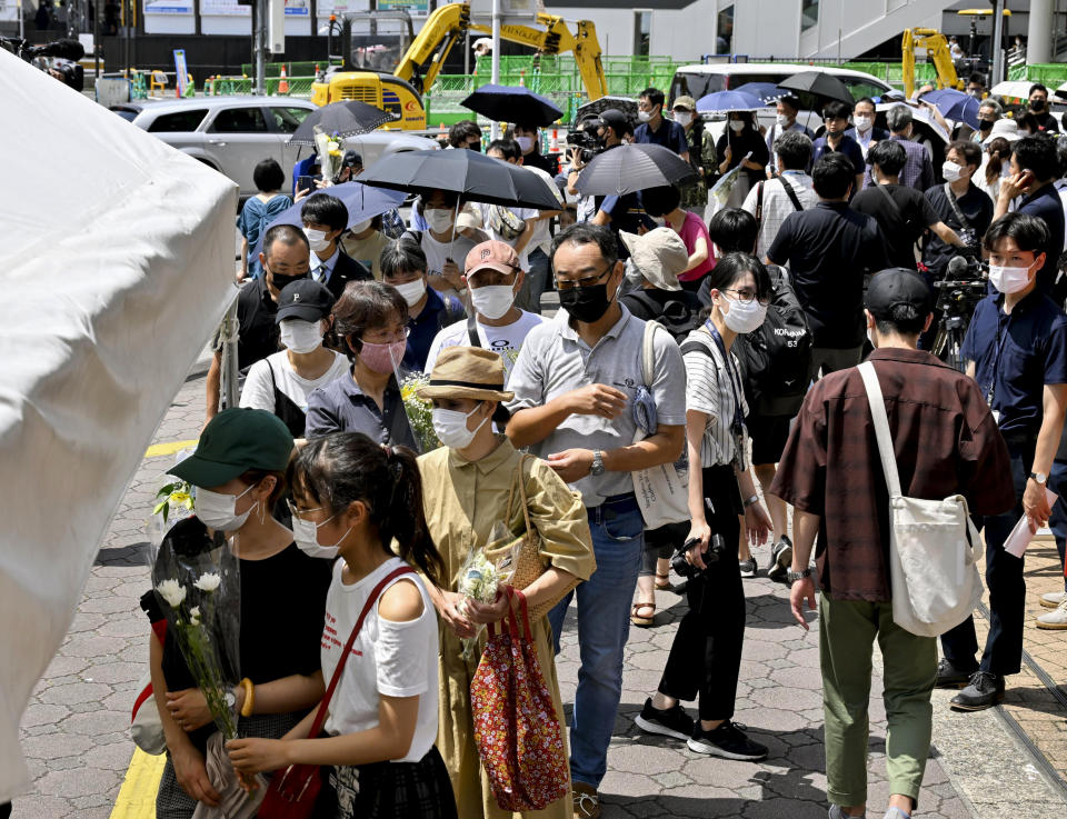 People wait in a line to offer flowers at a makeshift memorial near the scene where former Prime Minister Shinzo Abe was fatally shot while delivering his speech to support the Liberal Democratic Party's candidate during an election campaign in Nara, Saturday, July 9, 2022.(Kyodo News via AP)