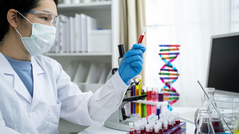 Female researcher looking at test tube with DNA statue in the background.