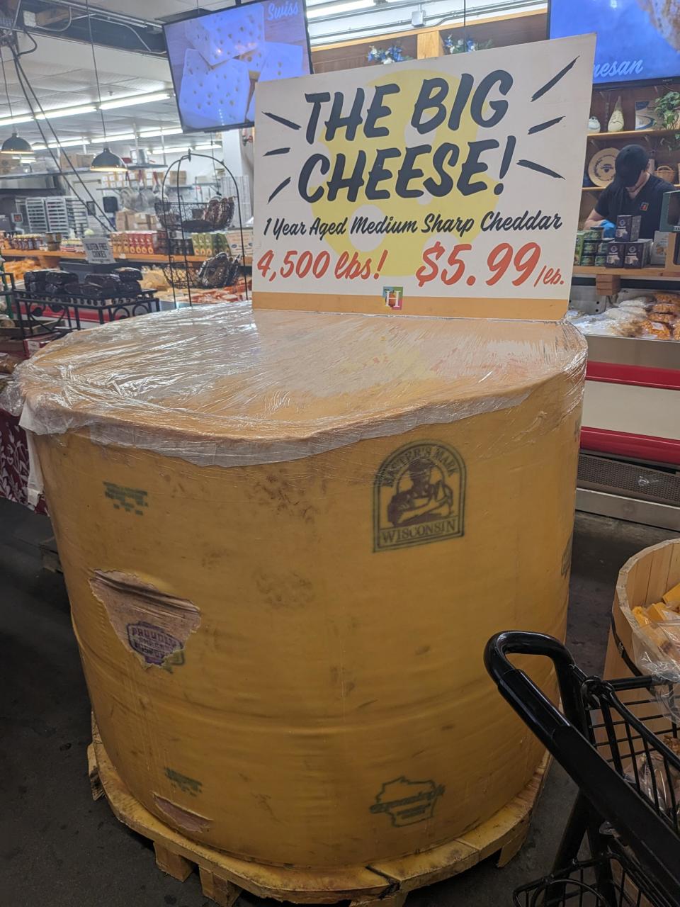 Giant wheel of cheddar cheese for sale at $5.99/lb, labeled "THE BIG CHEESE," weighing 4,500 lbs