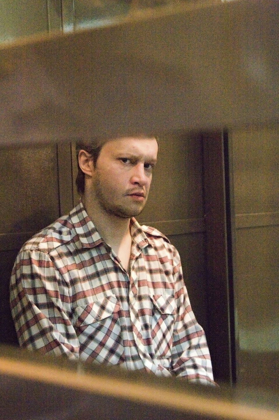 alexander pichushkin sitting in a defendants cage and looking to his right toward the camera lens