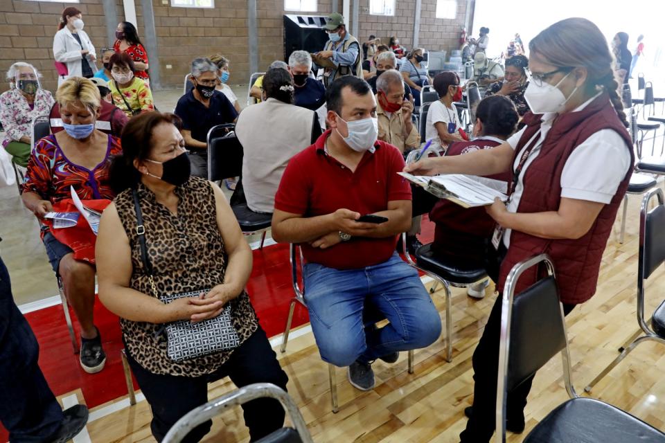 A masked woman with a clipboard, right, speaks to masked people seated at a vaccination site