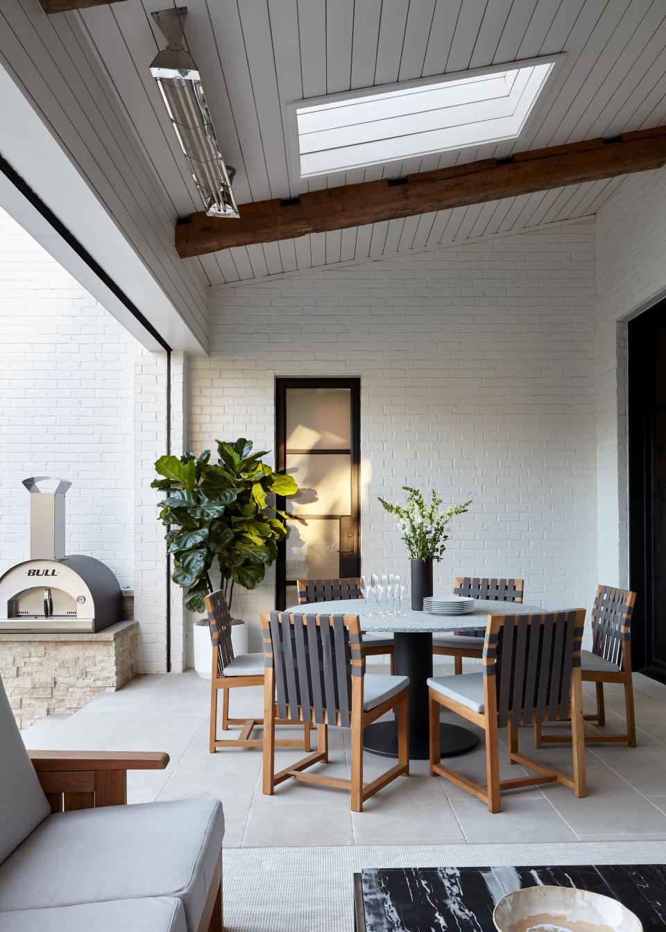 This outdoor deck gets year-round warmth thanks to an electric heater installed on the ceiling and a wood-burning fireplace (not pictured). The stone-topped round table and the teak chairs with woven backs are from Roda via 1stDibs.