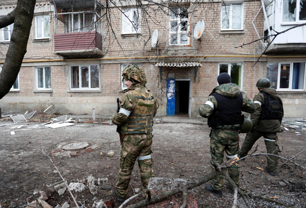 Militants of the self-proclaimed Donetsk People's Republic stand in front of an apartment building, which locals said was damaged by recent shelling, in the separatist-controlled town of Yasynuvata (Yasinovataya) in the Donetsk region, Ukraine February 24, 2022. REUTERS/Alexander Ermochenko