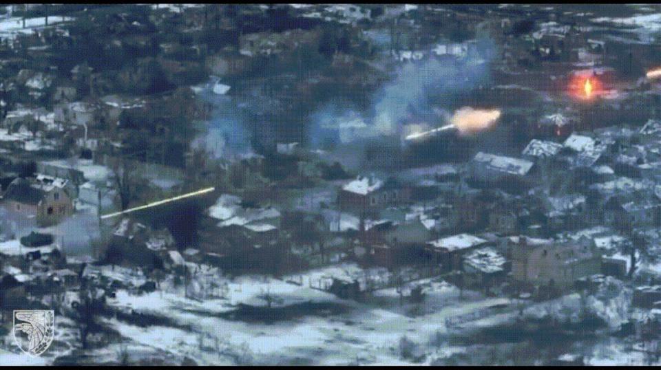 A moving image of an armored vehicle firing bright rounds down a street towards a target.