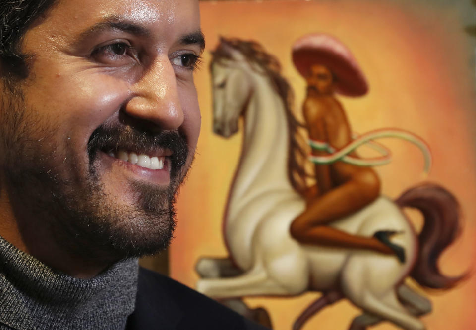 Mexican artist Fabian Chairez stands next to his painting showing Mexican Revolution hero Emiliano Zapata straddling on a horse nude, wearing high heels and a pink, broad-brimmed, during an interview at the Fine Arts Palace in Mexico City, Wednesday, Dec. 11, 2019. Mexico President Andres Manuel Lopez Obrador says he'll ask his culture minister to mediate a dispute over an effeminate painting of Zapata. (AP Photo/Marco Ugarte)