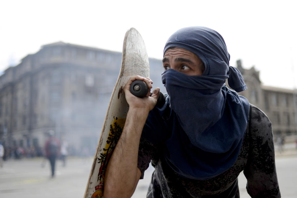 An anti-government protester peers out from behind his skateboard during clashes with police in Valparaiso, Chile, Friday, Oct. 25, 2019. A new round of clashes broke out Friday as demonstrators returned to the streets, dissatisfied with economic concessions announced by the government in a bid to curb a week of deadly violence.(AP Photo/Matias Delacroix)