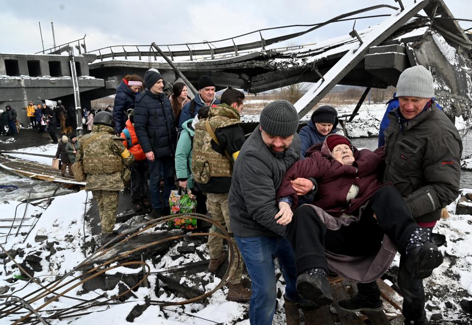 Two men help an elderly woman across a destroyed bridge as she evacuates Irpin. 