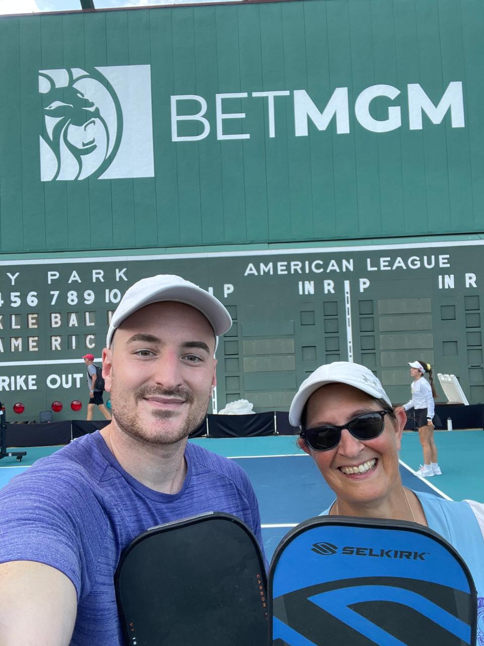 Beth Atkinson, right, of Ward Park Pickleball Club in Marlborough, poses with playing partner Chris Coroniti in front of the Green Monster at Fenway Park on July 12 during the Pickle4 Ballpark Series tournament in Boston.