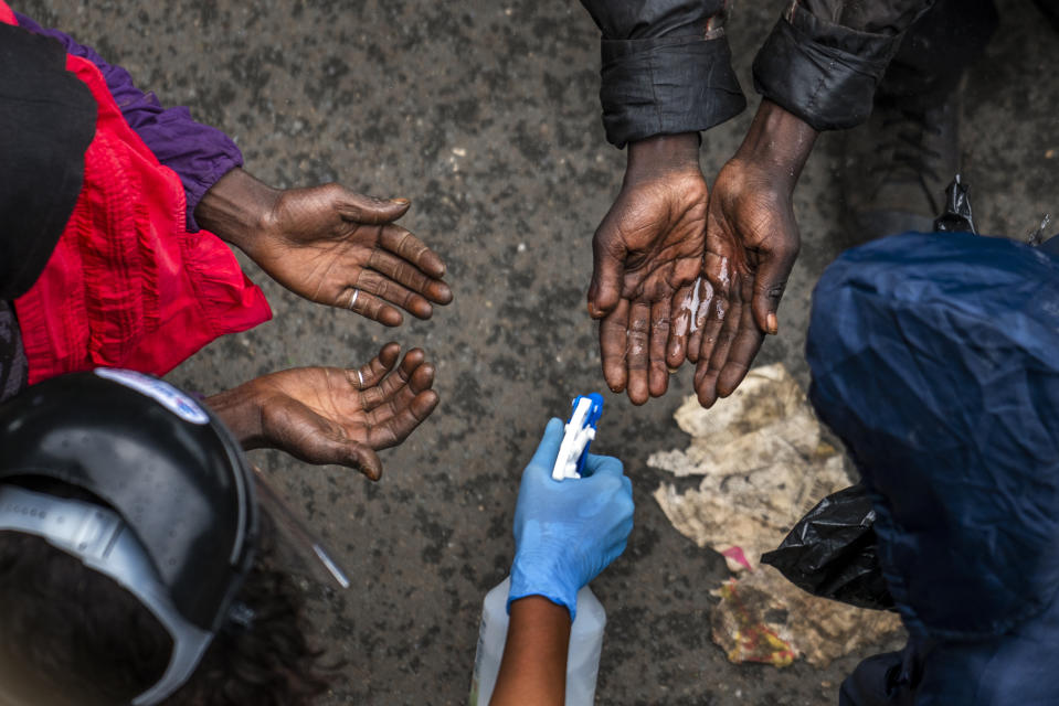 Indigentes se desinfectan las manos antes de recibir comida en Johannesburgo el 13 de abril del 2020, durante la pandemia del coronavirus. (AP Photo/Jerome Delay)