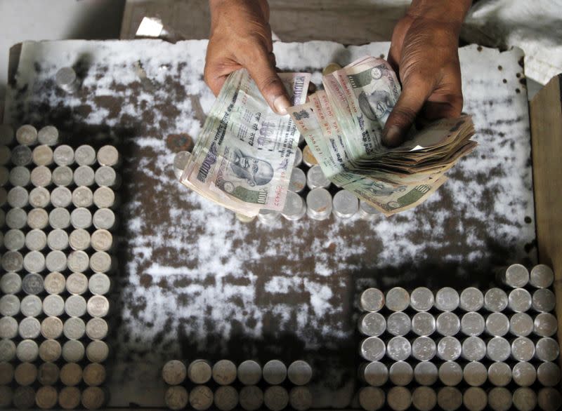 A man exchanging damaged Indian currency counts 100 rupee notes along a roadside in Kolkata