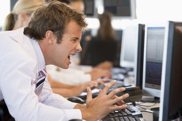 A visibly angry and frustrated investor looking at losses on his computer monitor.