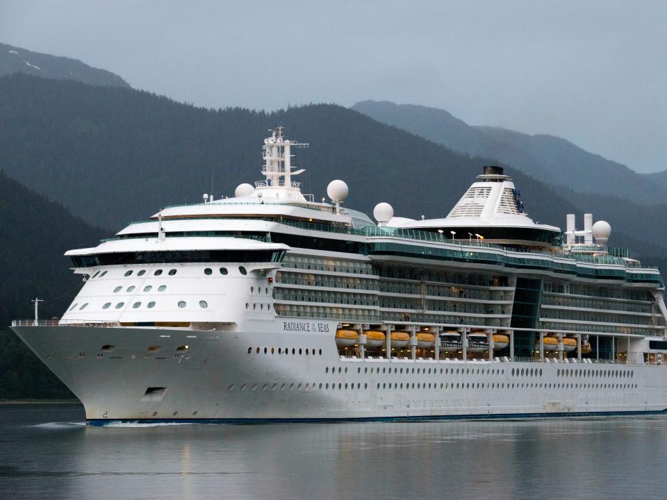 Radiance of the Seas, sailing near the South Franklin dock, Juneau, Alaska, in 2016. There are mountains with a blue-gray hue behind the ship.