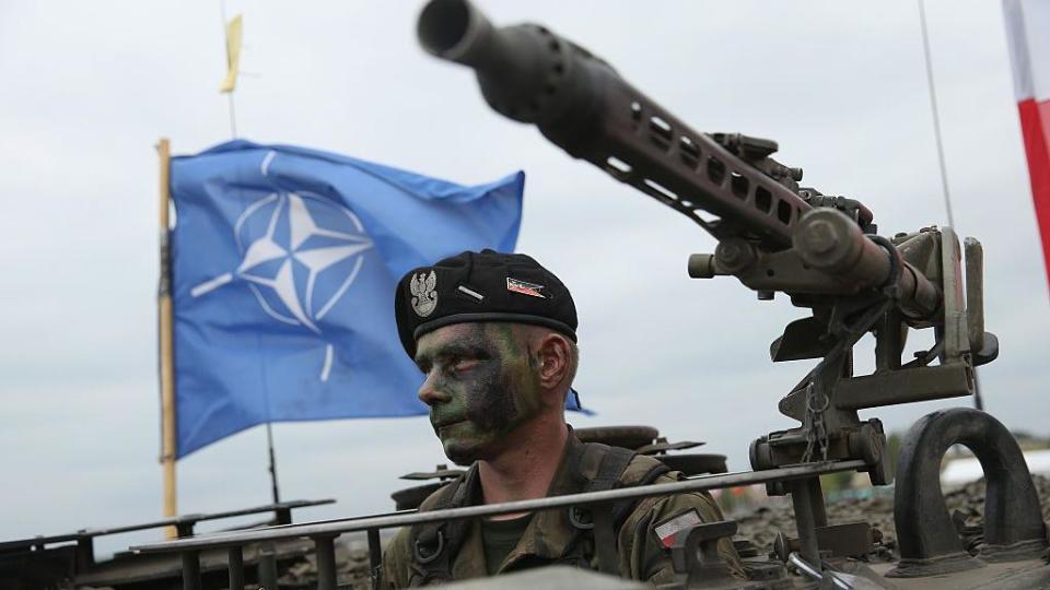 Un soldado de Polonia dentro de un tanque y con la bandera de la OTAN a sus espaldas 