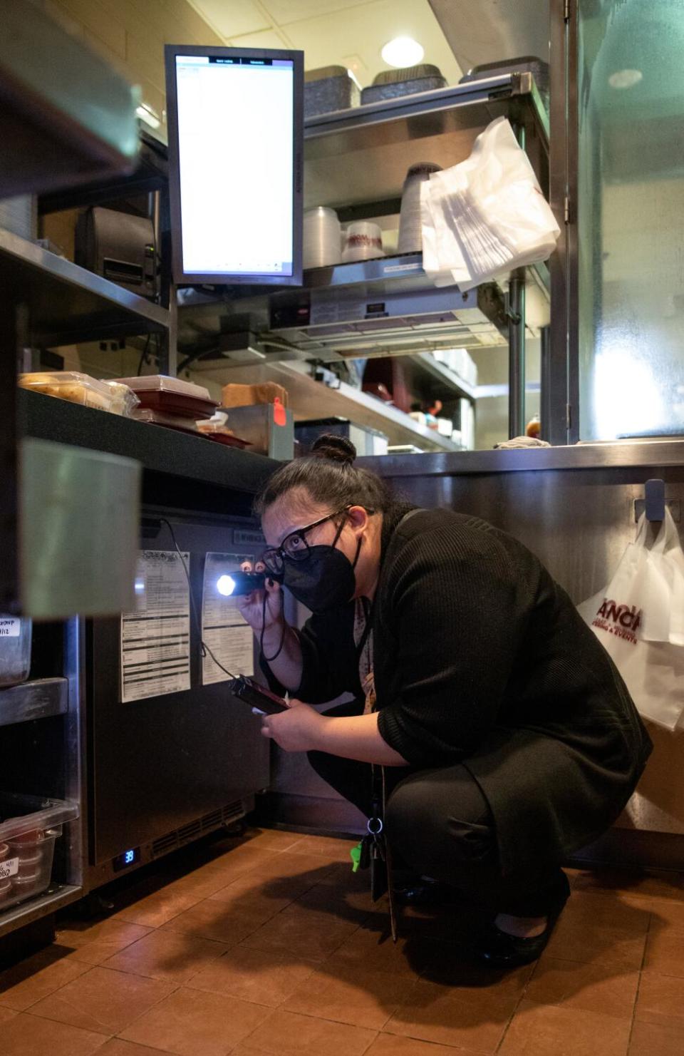 Ngoc McShane, environmental health specialist, uses a flashlight to look under shelving and inside storage areas.