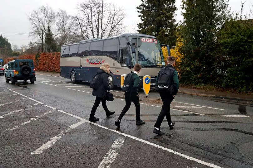 Teenage boys with school bags walk to a bus stop in Hartley Wintney