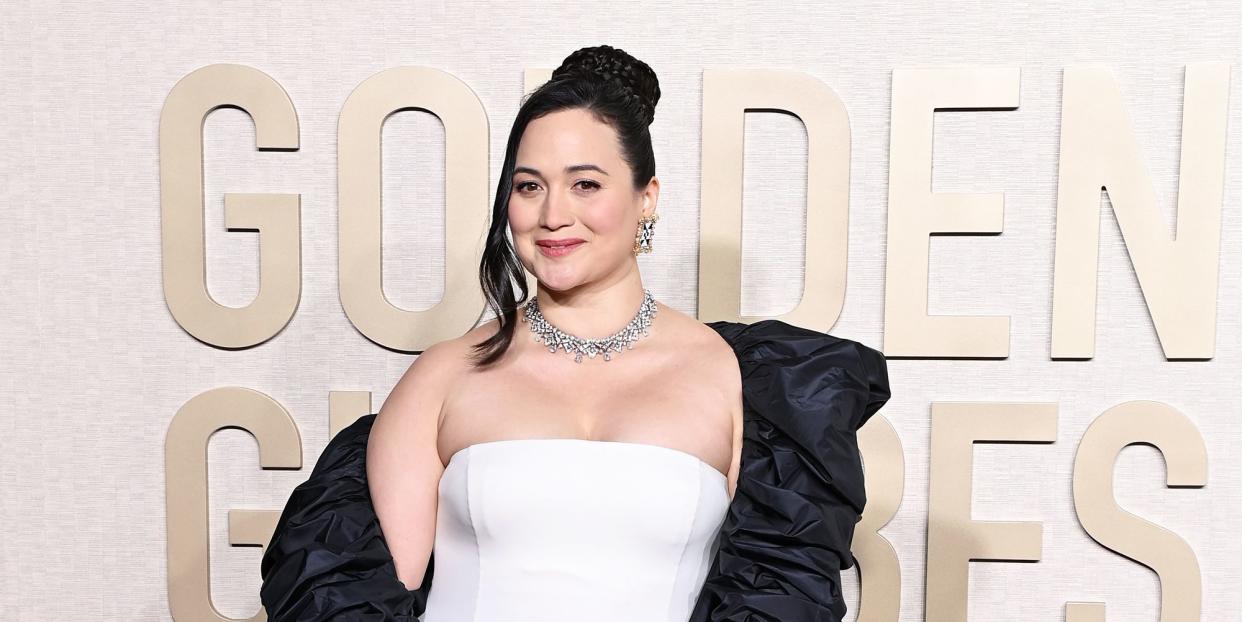 lily gladstone wearing a white dress and black coat at the golden globes