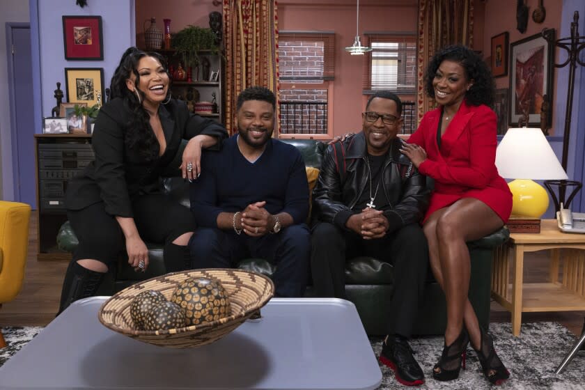 Four people smiling and sitting on a black couch in a living room