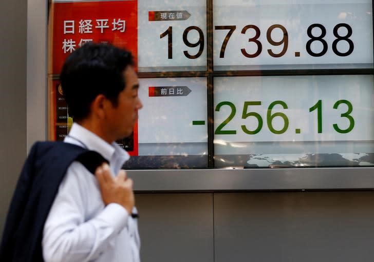 FILE PHOTO - A man walks past an electronic board showing Japan's Nikkei average outside a brokerage at a business district in Tokyo, Japan August 9, 2017. REUTERS/Kim Kyung-Hoon