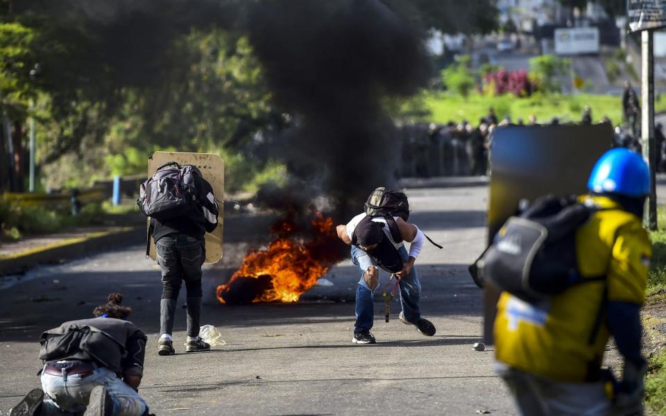 Anti-government activists skirmish with riot police during a protest in Caracas - Credit: AFP