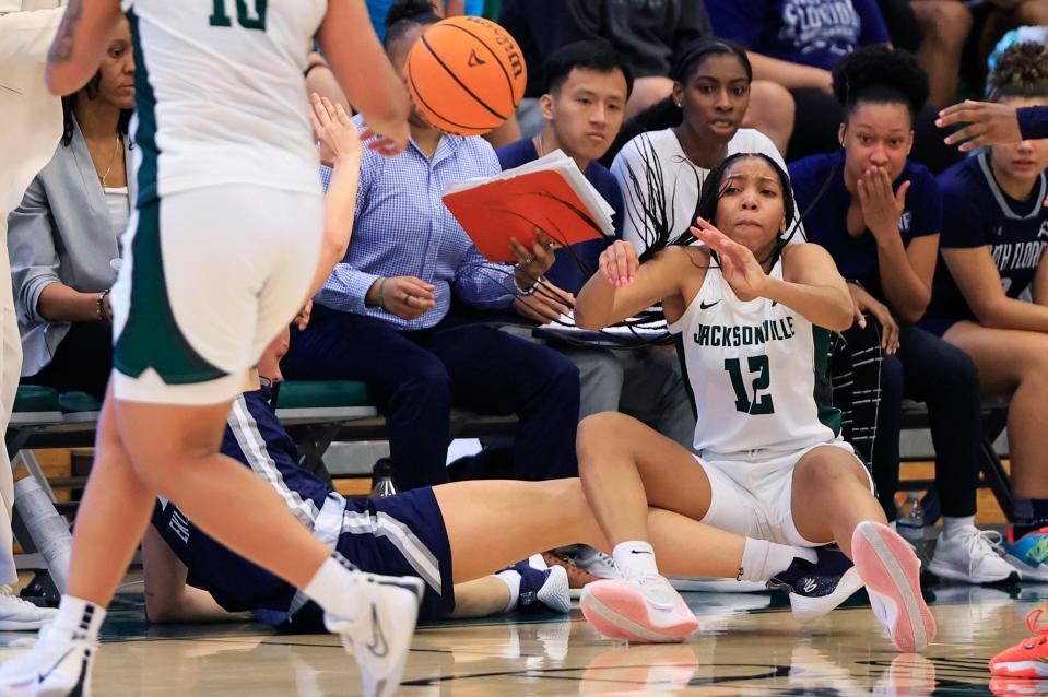 Jacksonville University guard Jalisa Dunlap (12) saves the ball before passing to guard Edyn Battle (10) as North Florida forward Selma Eklund (13) loses her footing near her team's bench during the fourth quarter of their game on Saturday JU's Swisher Gym.