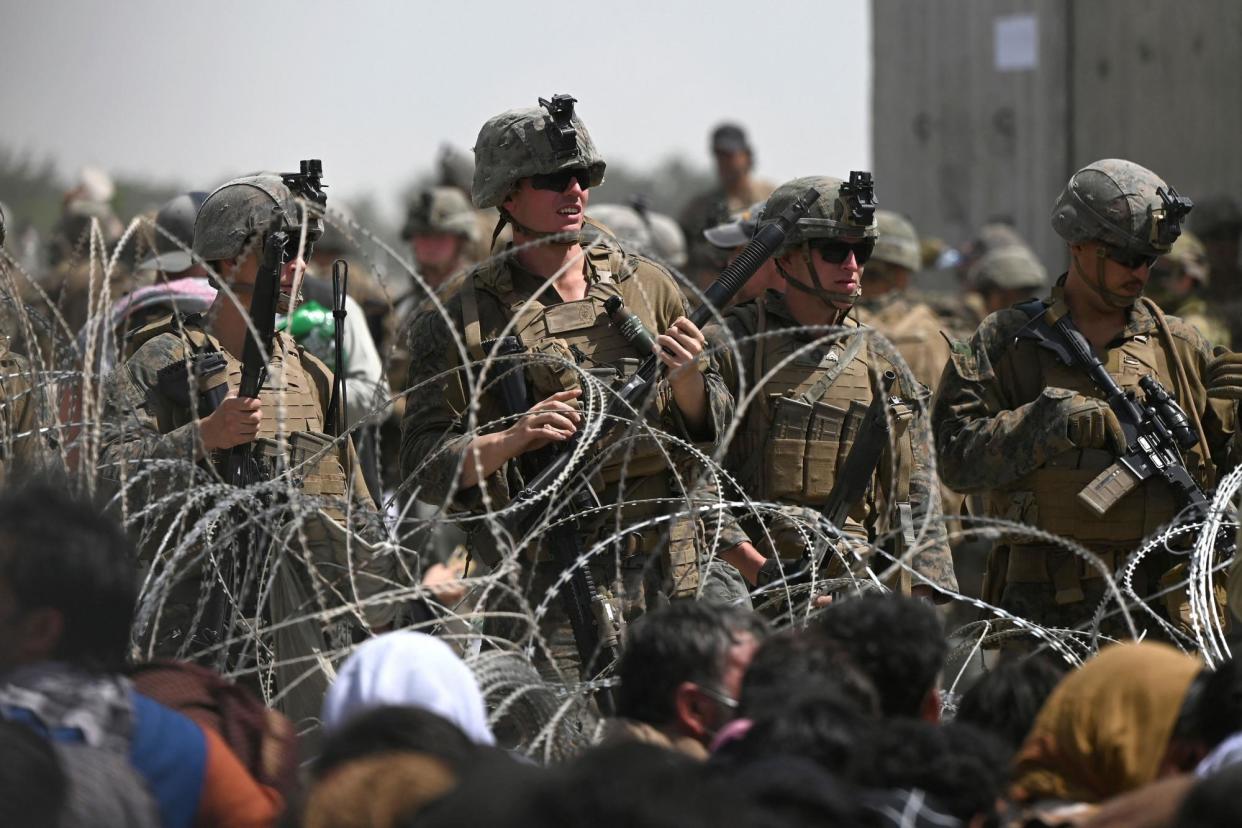 <span>US soldiers stand guard behind barbed wire as Afghans sit on a roadside near the military part of the airport in Kabul on 20 August 2021.</span><span>Photograph: Wakil Kohsar/AFP/Getty Images</span>