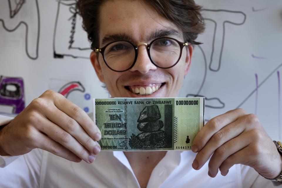 Eric Martinez, a graduate student in the Department of Brain and Cognitive Science at the Massachusetts Institute of Technology, holds a Zimbabwean $10 trillion bill, Friday, Sept. 9, 2022, in Cambridge, Mass. Martinez, who also has a law degree from Harvard University, shared the literature Ig Nobel with Francis Mollica and Edward Gibson for analyzing what makes legal documents unnecessarily difficult to understand. The 32nd annual Ig Nobel prize ceremony on Thursday, Sept. 15, 2022, was for the third year in a row a prerecorded affair because of the lingering effects of the coronavirus pandemic. (AP Photo/Michael Dwyer)
