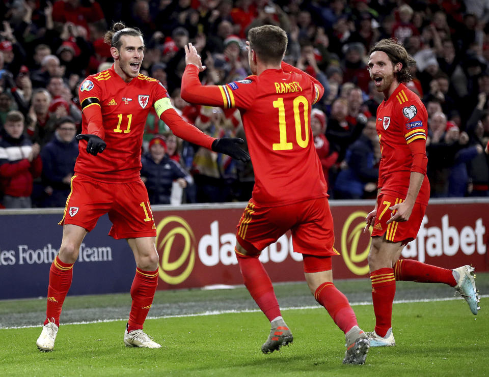 Wales' Aaron Ramsey celebrates scoring his side's first goal of the game against Hungary, with team-mates Gareth Bale, left, and Joe Allen, right, during their UEFA Euro 2020 Qualifying soccer match at the Cardiff City Stadium, in Cardiff, Wales, Tuesday Nov. 19, 2019. (Nick Potts/PA via AP)