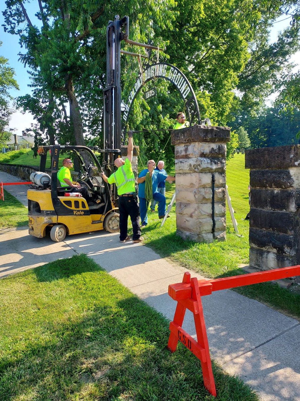 Members of the Granville Township crew assist blacksmith Kelly Wetzel in taking down the arch of the Memorial Gate so that it can be sent along with the gates for restoration at Wetzel's shop, Blackhand Forge.