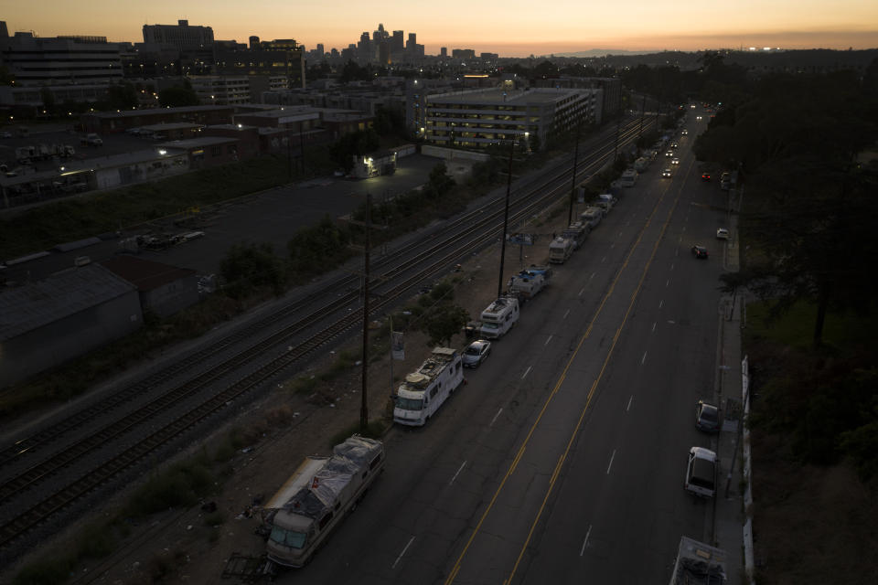 A line of weathered homeless RVs stretches along a street as the sun sets behind the Los Angeles skyline, Monday, Sept. 18, 2023. There is no single reason why Los Angeles became a magnet for homelessness. Two contributing factors: Soaring housing prices and rents punish those with marginal incomes, and a long string of court decisions made it difficult for officials to clear encampments or relocate homeless people from parks and other public spaces. (AP Photo/Jae C. Hong)
