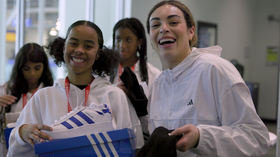 Sarah Nurse poses with a member of the Black Girl Hockey Club Canada community holding up an adidas Superstar running shoe during Nursey Night at a PWHL Toronto game