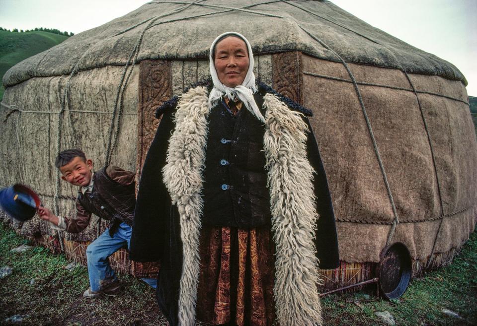 A boy, Muratepic, pops out of a yurt just as this Chinese woman, Gurjan, a mother of eight, is having her portrait made in Urumqi, Xinjiang Province, China, in 1985.