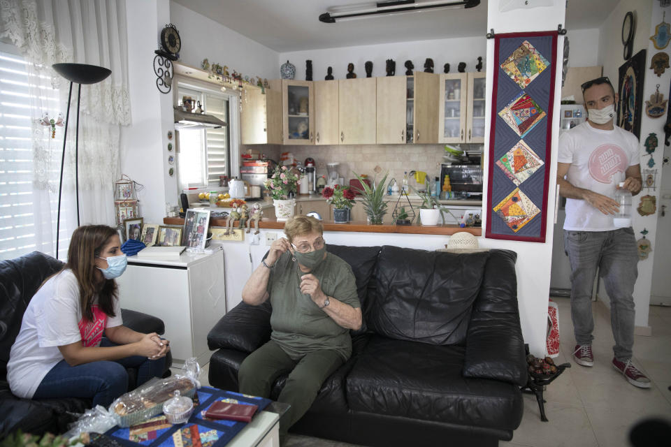 Itamar Glazer, right, Israeli volunteer Sharon Yaron, left, and 85-year-old Holocaust survivor Sara Weinsten, visit in Yavne, Israel, Thursday, Oct. 8, 2020. For thousands of older Israelis like Weinsten, being housebound alone during Israel's second nationwide lockdown due to the coronavirus pandemic is difficult and depressing. But each week ahead of the Jewish Sabbath, which starts on Friday at sundown, a home-baked cake is delivered by one of thousands of volunteers bringing pastries to home-bound older Israelis. (AP Photo/Sebastian Scheiner)