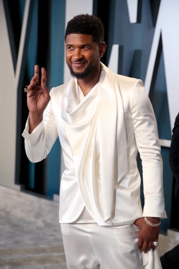 Usher in a stylish white suit with a draped lapel waves at the camera