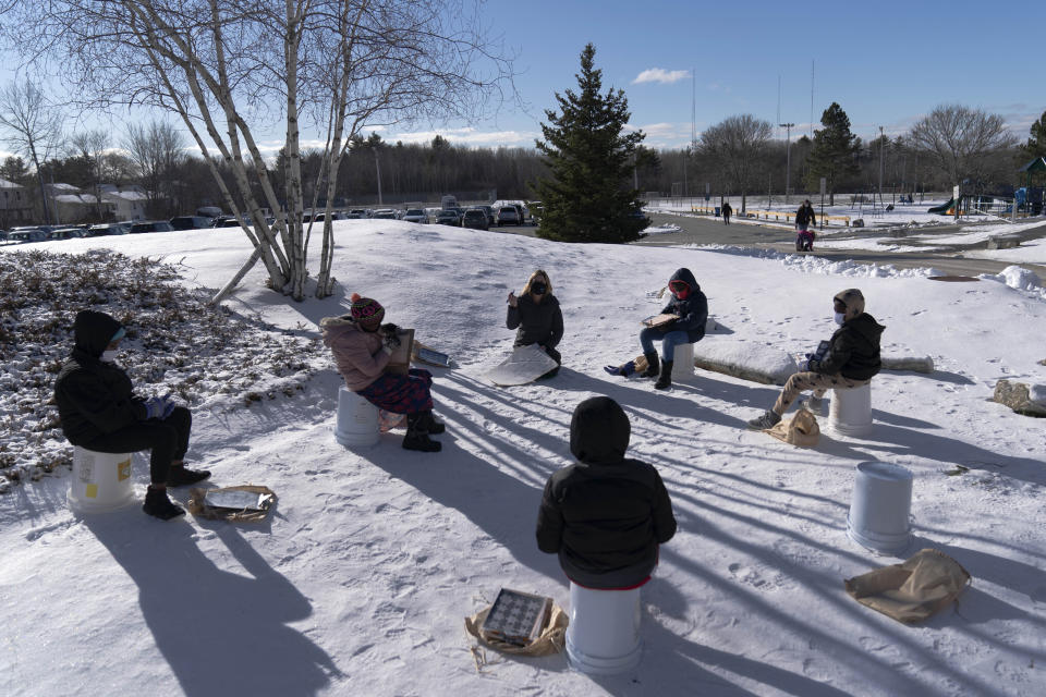 In this Monday, Dec. 8, 2020 photo, a fourth grade class uses upside-down buckets for seats as they study outside at the Gerald Talbot School, in Portland, Maine. The outdoors is considered to be the healthiest, safest place for kids to be during the pandemic. (AP Photo/Robert F. Bukaty)