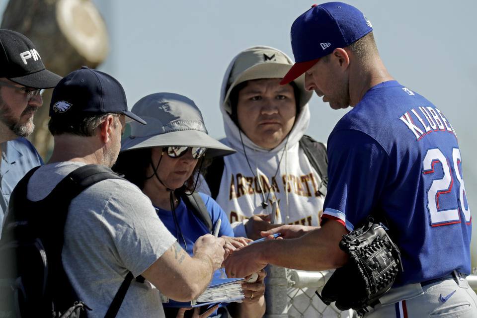 Texas Rangers pitcher Corey Kluber, right, gives autographs during spring training baseball practice Friday, Feb. 14, 2020, in Surprise, Ariz. (AP Photo/Charlie Riedel)