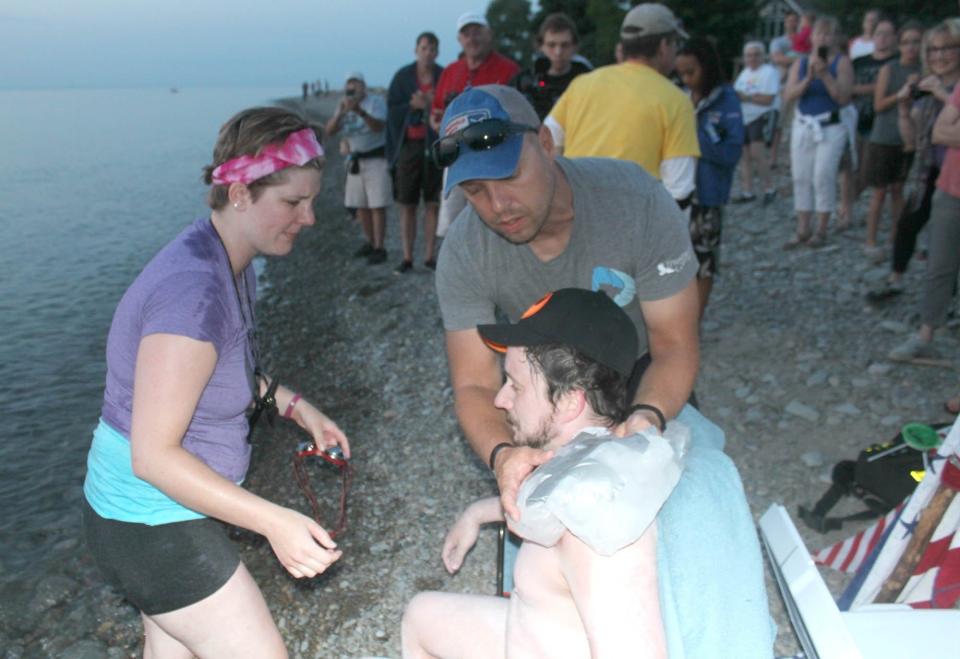 Greg Roberts, foreground, gets his shoulders iced by Josh Heynes, manager of Lake Erie Open Water Swimming Association, as Roberts' girlfriend, Candace Jeska, left, watches on Freeport Beach in North East in 2018, when Roberts completed his swim across Lake Erie.