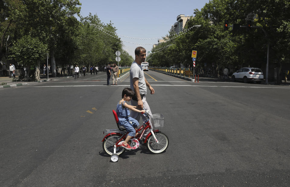 In this Friday, May 17, 2019 photo, a man with his daughter cross Enqelab-e-Eslami (Islamic Revolution) street in downtown Tehran, Iran. (AP Photo/Vahid Salemi)