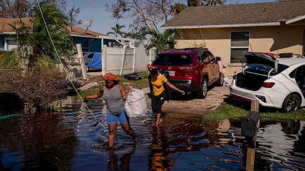 PHOTO: Atlas Dorlean, left, carries a bag of salvaged belongings through floodwater left after Hurricane Ian tore through the Harlem Heights area of Fort Myers, Fla. Sept. 29, 2022. (Hilary Swift/The New York Times via Redux)