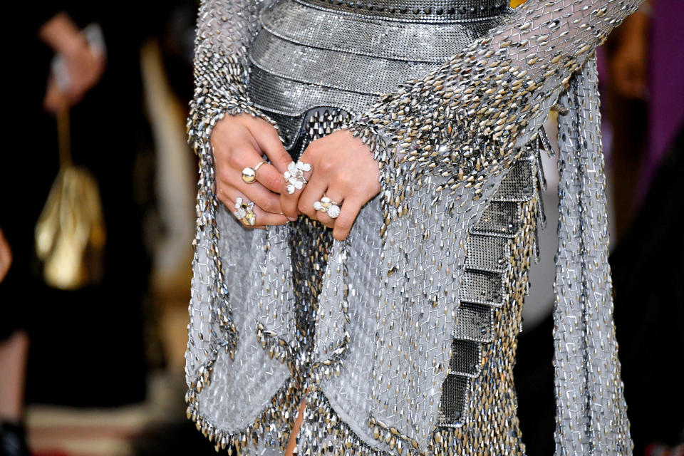 Close-up of a Zendaya's midsection in a metallic chainmail dress with their hands clasped in front, adorned with rings at the Met Gala