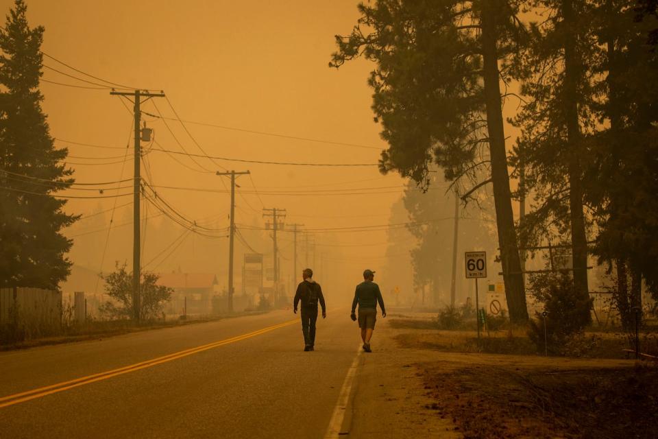 Two men walk along a road in Scotch Creek, B.C., as wildfire smoke fills the air on Aug. 19, 2023.
