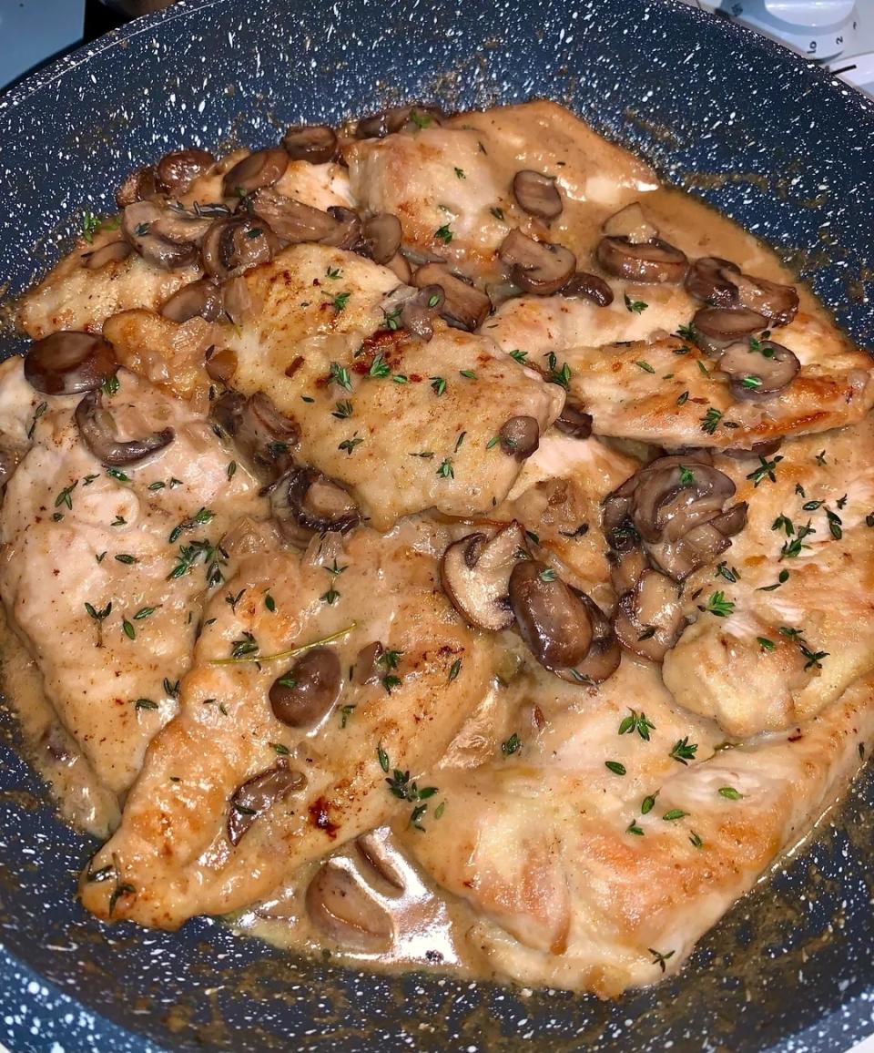 Chicken breast pieces are cooked in a skillet with mushrooms and a creamy sauce, garnished with herbs