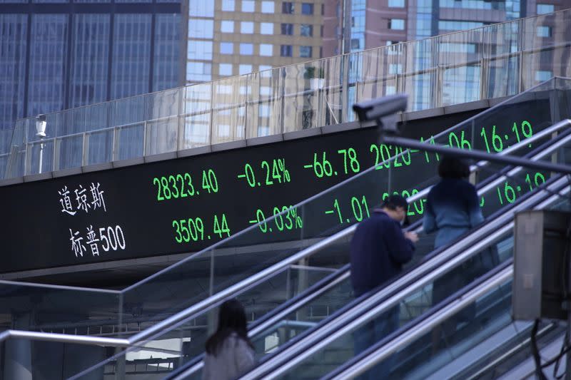 People wearing masks, following the coronavirus disease (COVID-19) outbreak, are seen near an electronic board showing Dow Jones and S&P 500 stock indexes, at the Lujiazui financial district in Shanghai