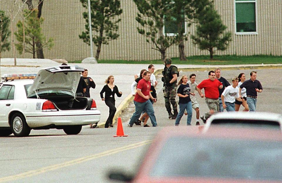 Students run from Columbine High School run under cover from police 20 April 1999 in Littleton, Colorado (AFP via Getty Images)