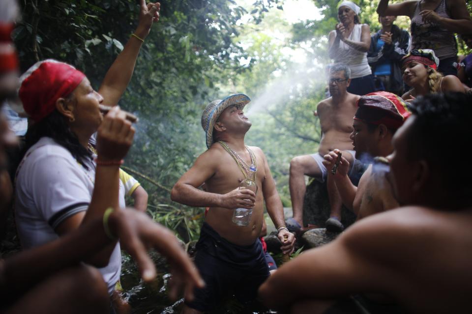 In this photo taken Oct. 12, 2019, Juan Carlos Paso sprays water from his mouth on others during a ceremony on Sorte Mountain where followers of indigenous goddess Maria Lionza gather in Venezuela's Yaracuy state. The cult of the goddess is hundreds of years old and draws on elements of the Afro-Caribbean religion Santeria and indigenous rituals, as well as Catholicism. (AP Photo/Ariana Cubillos)