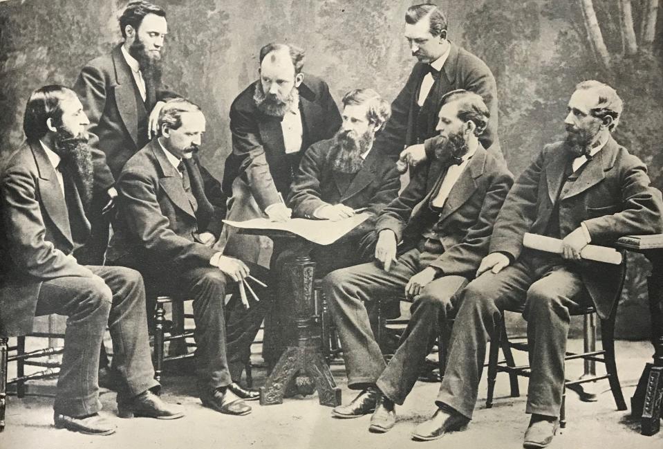 Eight of the charter members of the Cincinnati chapter of the AIA posed for this picture. Samuel Hannaford is standing at left. James W. McLaughlin is bending over the table and James Keys Wilson is sitting with his hand on the table.