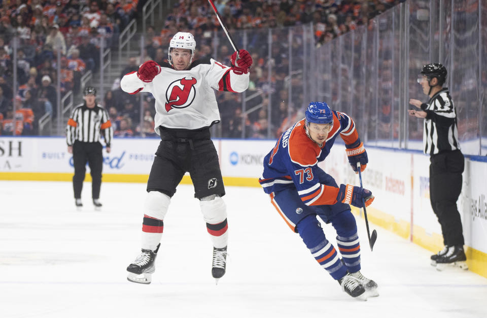 New Jersey Devils' Nathan Bastian (14) dodges a hit from Edmonton Oilers' Vincent Desharnais (73) during first-period NHL hockey game action in Edmonton, Alberta, Sunday, Dec. 10, 2023. (Jason Franson/The Canadian Press via AP)