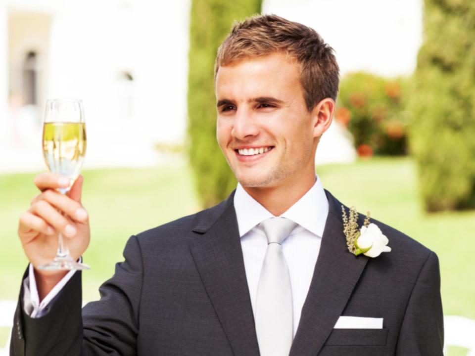 Un padrino sonríe y brinda con una copa de champán en una boda (Getty Images) (Getty Images)