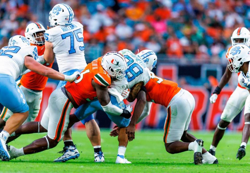 Miami Hurricanes defensive linemans Leonard Taylor III (56) and Nyjalik Kelly (32) bring down North Carolina Tar Heels running back Omarion Hampton (28) during the fourth quarter of an ACC conference football game at Hard Rock Stadium on Saturday, October 8, 2022 in Miami Gardens, Florida..